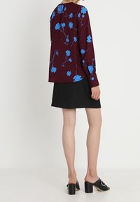 Blouse florale bordeaux avec des fleurs bleues, manches longues et coupe décontractée, associée à une jupe noire trapèze et des mules noires à talons.
