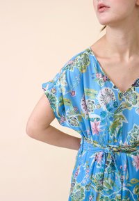 Robe florale bleu clair avec un décolleté en V, des manches courtes et une taille froncée. Présente des motifs floraux multicolores et une texture douce.