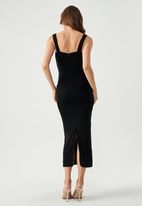 Black, form-fitting dress with wide straps, a low back, and a thigh-high slit. Made of soft fabric with a smooth texture.
