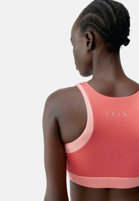 Sportmelltartó korall színű gradiensben, sima textúrával, versenyhát kialakítással és diszkrét logórésszel a háton.