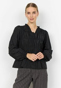 Fekete blúz ráncolt textúrával, V-nyakkal és puffos ujjakkal. Szürke csíkos nadrággal párosítva. Sima anyag, könnyű kialakítás.