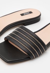 Sandales à glissière noires avec une tige en cuir texturé et trois bandes métalliques argentées sur la bride. Bout carré et semelle plate.