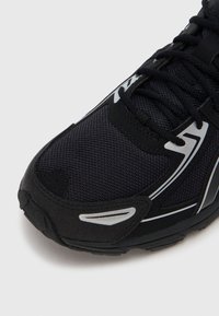 Čierna športová obuv s textúrovaným sieťkovým zvrškom, reflexnými striebornými akcentmi a polstrovanou podrážkou. Šnúrky sú čierne a pevne tkané.