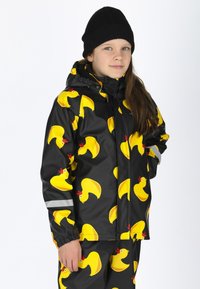 Schwarze wasserdichte Jacke mit gelben Gummientenmustern, verstellbare Kapuze und reflektierenden Streifen an den Ärmeln. Kombiniert mit passenden Hosen.