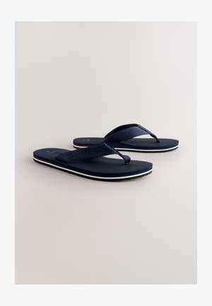 Marinblå flip-flops med en strukturerad rem, en flat sula och vita och röda accentstripes. Lätt och avslappnad design för sommarslitage.