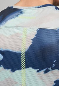 Haut de performance à manches courtes en bleu et gris clair avec une texture en maille. Présente un motif abstrait et une bande réfléchissante verticale au dos.