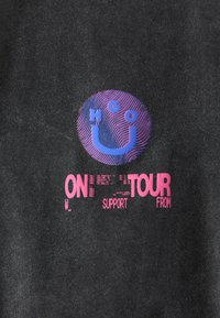 Black fabric featuring a circular graphic in blue and pink, including the text “ON TOUR” and "SUPPORT" with a wavy line pattern.