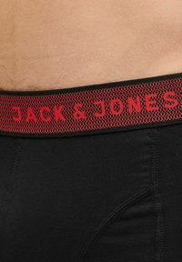 Schwarze Boxershorts für Herren mit einem strukturierten elastischen Bund und rotem "JACK & JONES" Schriftzug. Glattes Material und figurbetontes Design.