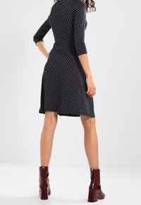 Robe à pois bleu marine avec des manches trois quarts, un ourlet évasé et une texture douce, associée à des bottines bordeaux à talon carré.