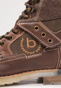 Bota de cuero marrón y tela con puntera redonda, ojales metálicos y costuras en contraste. Presenta un logotipo bordado y acentos texturizados.