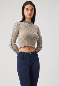 Gestrickter Crop-Pullover aus mehrfarbigem Garn mit gewelltem Saum und Ärmeln. Kombiniert mit dunkelblauen, figurbetonten Jeans mit klassischer Tasche.