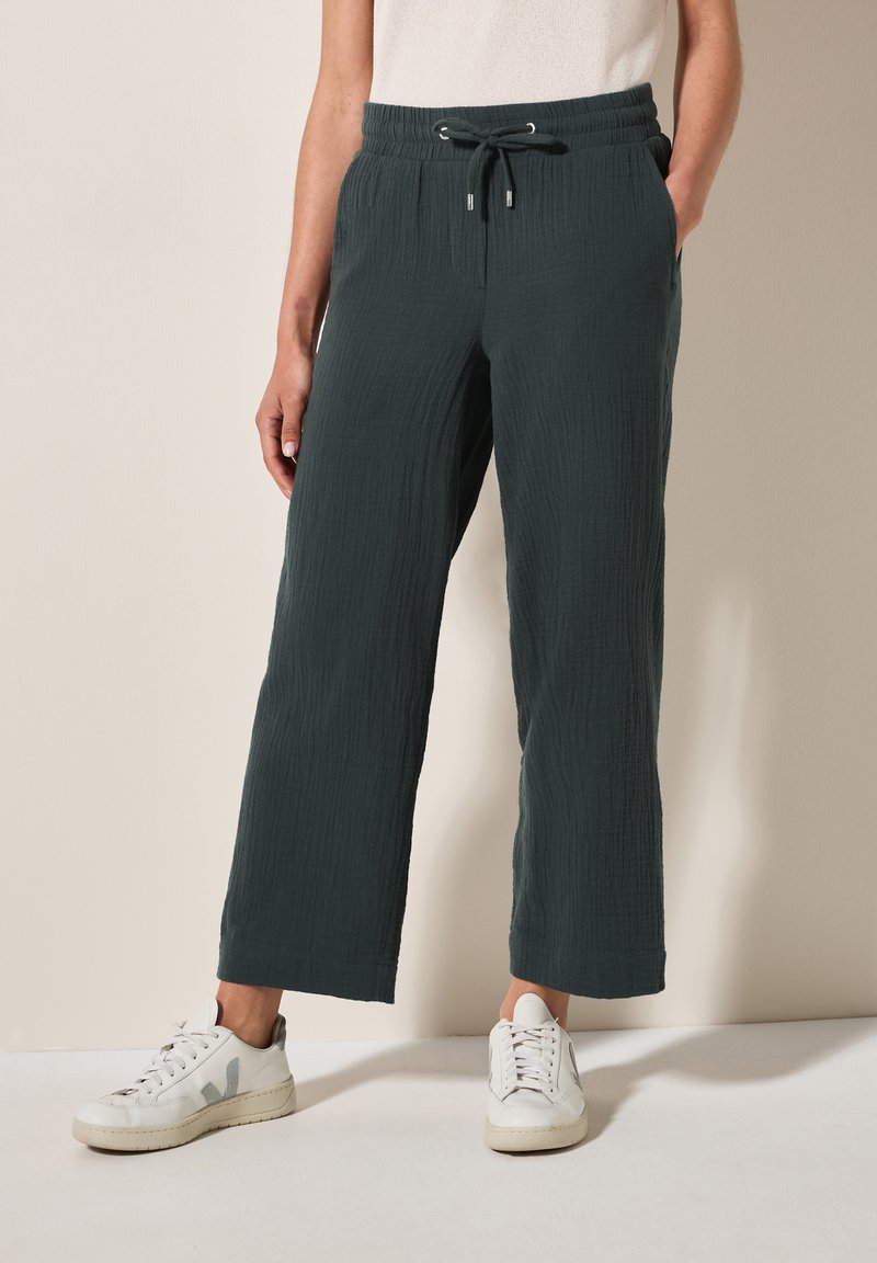 Dark green, textured wide-leg pants with an elastic waistband and drawstring. Styled with white sneakers, showing a casual look.