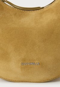 Borsa a spalla in suede giallo senape con finitura liscia e logo argento. Presenta una forma curva e dettagli cuciti lungo il bordo.