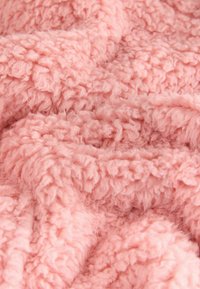 Flauschiger rosa Plüschstoff mit einer weichen, strukturierten Oberfläche, die ein welliges, zerknittertes Aussehen hat. Ideal für Decken oder gemütliche Bekleidung.