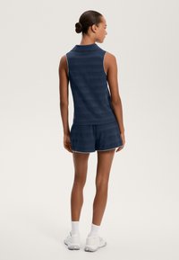 Mornarsko brezrokavnik s teksturiranim prugastim vzorcem, v kombinaciji z ujemajočimi se kratkimi hlačami. Obe imata bele obrobe.