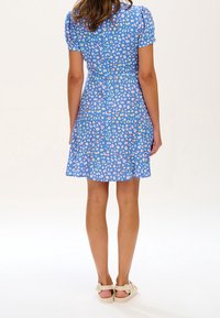 Kortärmad, blå klänning med en lekfull, färgglad leopardtryck. Urtalad kjol, knälång, tillverkad av lättviktsmaterial. Knäppning bak med knapp.