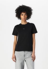 Svart bomull t-skjorte med korte ermer og rund hals, med en liten logo på brystet. Brukt sammen med lysegrå jeans.