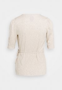 Haut beige à manches courtes avec une coupe décontractée, mettant en avant une ceinture à nouer à la taille et des épaules froncées pour un look texturé.