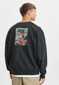 Mustast dressipluusist, millel on graafiline trükk seljal, kujutades tegelast klaasi hoidmas, värvikate ja tekstuuridega detailidega.