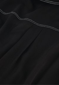 Zwart stof met een gladde textuur heeft contrasterende witte stiksels langs de naden en een reeks plooien voor extra ontwerpelement.