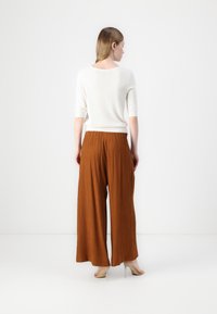 Witte top met driekwartmouwen, gecombineerd met brede, roestkleurige, gestructureerde broek. De outfit heeft een relaxte pasvorm en lichte stretch.