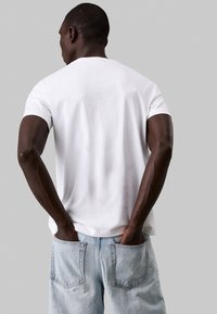 Maglietta bianca in cotone con maniche corte, vestibilità comoda, scollo rotondo, indossata con jeans in denim azzurri chiari caratterizzati da grandi tasche posteriori.