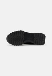 Black sneaker sole featuring a textured rubber surface with deep treads and Calvin Klein branding. Rounded toe and sturdy heel.