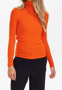 Haut à col roulé côtelé orange avec manches longues, coupe ajustée et texture lisse. Associé à un pantalon noir, créant un contraste visuel.