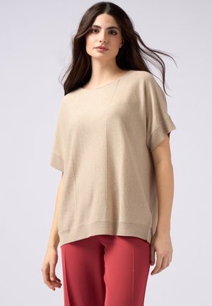 Top corto a maniche corte beige a coste con finitura liscia, caratterizzato da una vestibilità ampia e una sottile trama, abbinato a pantaloni rossi.