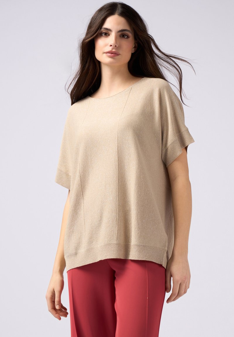 Top corto a maniche corte beige a coste con finitura liscia, caratterizzato da una vestibilità ampia e una sottile trama, abbinato a pantaloni rossi.