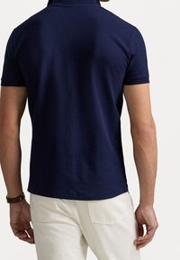 Námořnicky modré polo tričko s krátkými rukávy, z měkké bavlněné směsi a s límečkem. Tričko má čistý, minimalistický design.