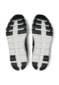 Semelle de chaussure de sport en noir et blanc, présentant un motif de grip en caoutchouc texturé et un design segmenté pour flexibilité et stabilité.