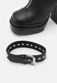Czarne ankle boots na platformie z błyszczącego sztucznego skóry, z detalem zamka błyskawicznego; zestawione z czarnym skórzanym paskiem z srebrnymi ćwiekami i klamrą.