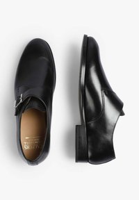 Zapatos de cuero negro con un diseño elegante, punta redondeada, sutil detalle de hebilla y un tacón bajo apilado. Textura suave y acabado pulido.