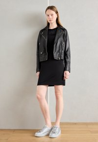 Veste de motard en cuir noir, robe noire ajustée et baskets argentées métalliques. Textures lisses et design minimaliste.