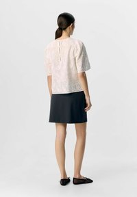 Haut à manches courtes en crème, avec une broderie florale et un détail en trou de clé au dos. Associé à une jupe noire lisse et des chaussures plates noires.