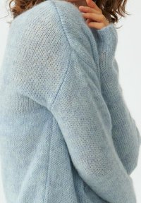 Jasnoniebieski, dzianinowy sweter wykonany z miękkiego, puszystego materiału. Posiada luźny krój, prążkowane mankiety oraz subtelną teksturę z wariacjami kolorystycznymi.