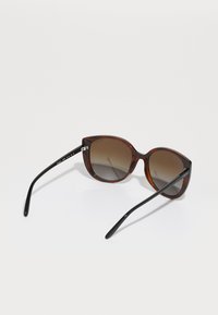 Ochelari de soare supradimensionați cu un model țestoasă, cu lentile maro degradé și brate negre, având un design elegant, cu ramă rotundă și detalii subtile ale logo-ului.