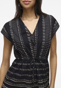 Abito nero con scollatura a V, maniche corte e vita con cordoncino. Presenta motivi dorati in linee orizzontali e verticali. Texture morbida.