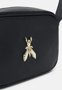 Borsa a tracolla in pelle nera con un'arricchitura a forma di insetto in oro. Texture liscia con un design strutturato e chiusura con zip.