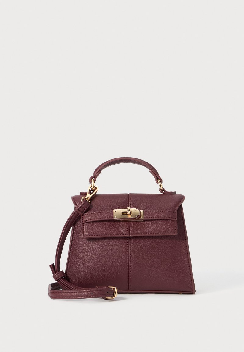 Burgundy leather handbag with a structured shape, detachable strap, top handle, gold hardware, and a front clasp closure.