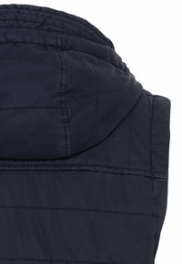 Gilet matelassé bleu marine sans manches avec une capuche attachée, montrant la partie supérieure du dos et des épaules.