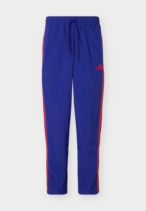 Pantaloni atletici blu con strisce laterali rosse e vita con coulisse, con un piccolo logo rosso sulla coscia superiore.