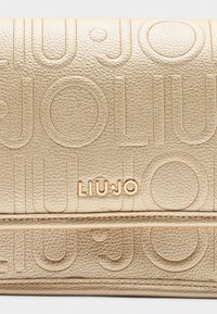 Portefeuille texturé en or avec logo "LIU JO" en relief et motifs circulaires. Il est composé de cuir lisse et a une forme rectangulaire élancée.