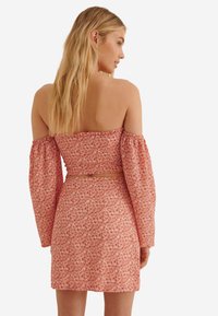 Röd blommig klänning med off-the-shoulder-design, långa puffärmar och figursydd midja, tillverkad av lättviktsmaterial.