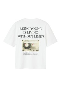 T-shirt en coton blanc avec un graphique de cassette audio au dos. Le texte indique « ÊTRE JEUNE, C'EST VIVRE SANS LIMITES » en lettres noires en gras.
