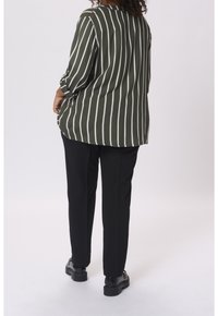 Chemise à rayures vertes avec des rayures verticales blanches, coupe décontractée, associée à un pantalon noir et des chaussures noires. Le tissu semble lisse.