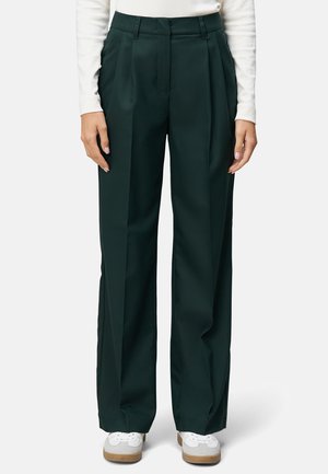 Pantalons plissés taille haute verts foncés à jambe large. Texture lisse, coupe ajustée, sans matériel visible, associés à des baskets blanches.