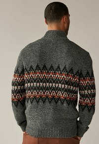 Gebreide trui in donkergrijs met een hoge kraag, voorzien van een chevronpatroon in zwart, wit en oranje op het bovenste gedeelte. Geverfd textiel.