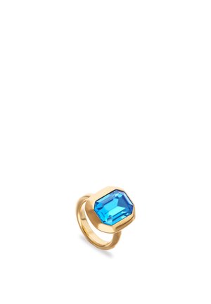 Anillo de oro con una gran piedra preciosa azul brillante tallada en esmeralda y engastada en un bisel hexagonal, mostrado sobre un fondo blanco.